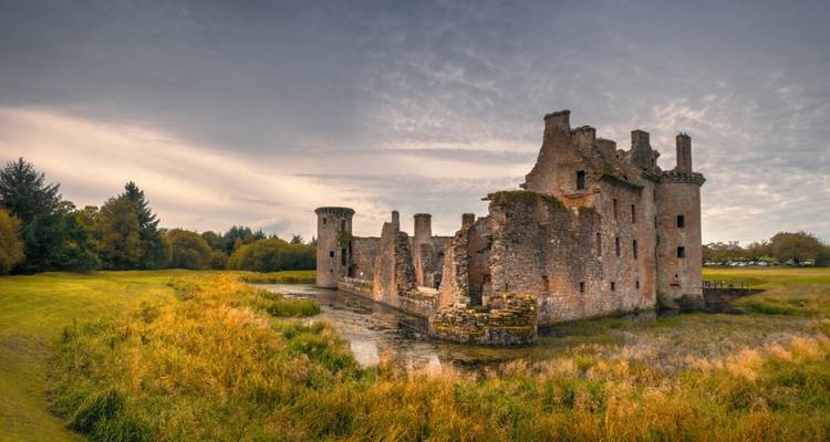 Ruïnes van een historisch kasteel in een grasrijk landschap.