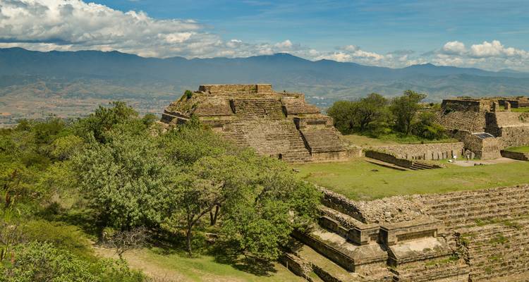 Ancient ruins on a plateau surrounded by trees with mountains in the distance.