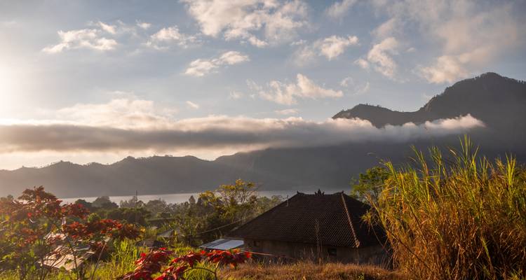 Scenic view of mountains, clouds, and a traditional thatched-roof building.