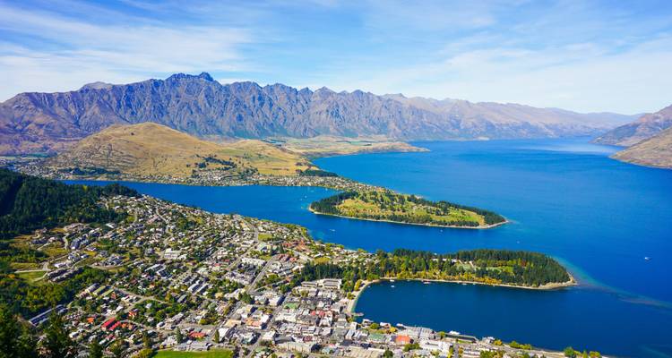 Weitläufige Luftaufnahme von Queenstown, tiefblauer See und raue Bergkette der Remarkables unter klarem Himmel