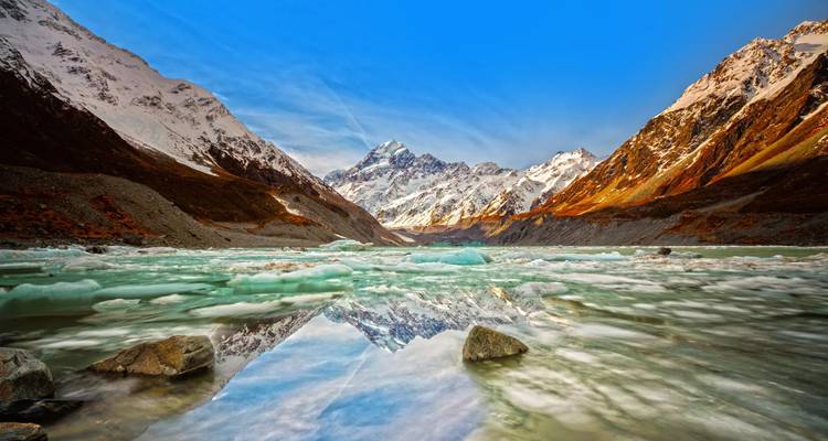 Der eisgefüllte Alpensee spiegelt schneebedeckte Gipfel und einen leuchtend blauen Himmel im Aoraki/Mount-Cook-Nationalpark wider.