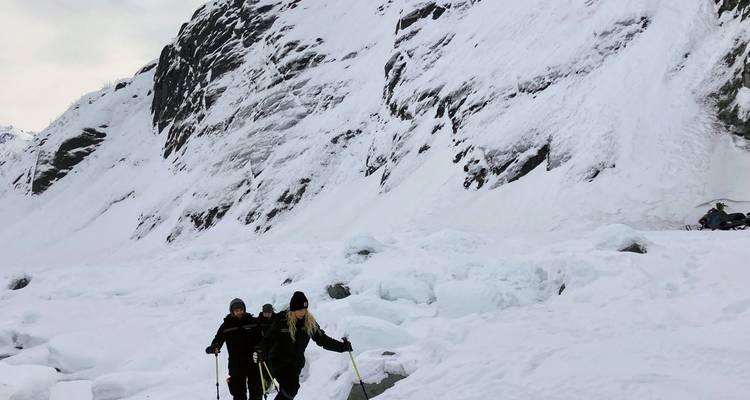 Wandelaars die een besneeuwde landschap doorkruisen met een torenhoge berg op de achtergrond.