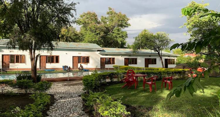 Petit lodge avec une piscine, des sentiers de jardin et des arbres sous un ciel partiellement nuageux.