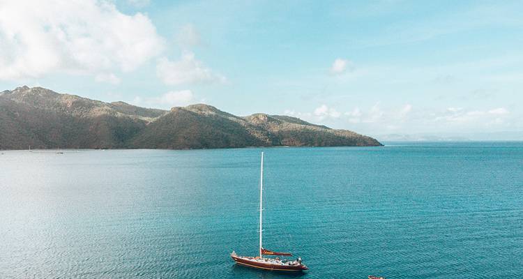 Velero solitario anclado en aguas turquesas con las exuberantes Islas Whitsunday al fondo.