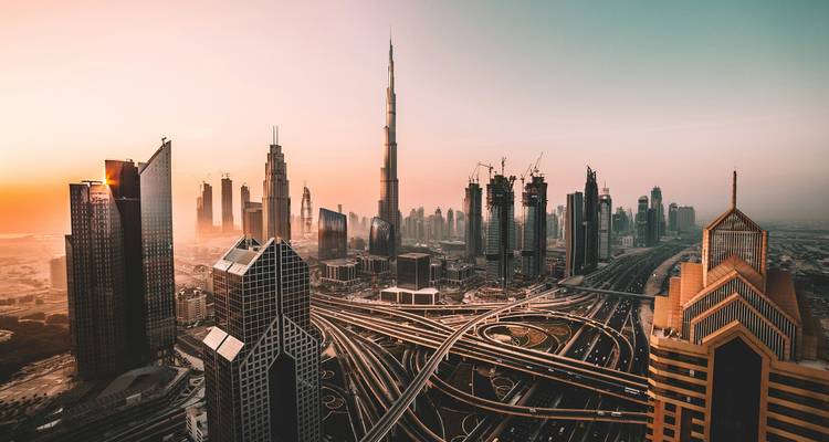 Skyline panorámica de Dubai con el Burj Khalifa y autopistas entrelazadas en un amanecer brumoso.