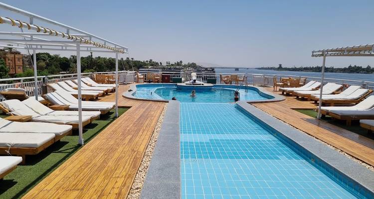 Pont de la piscine d'un bateau de croisière sur le Nil avec des chaises longues, une piscine de nage et une vue sur le fleuve bleu par une journée dégagée.