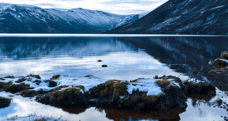 Sereen meer omringd door besneeuwde bergen en stukken gras.