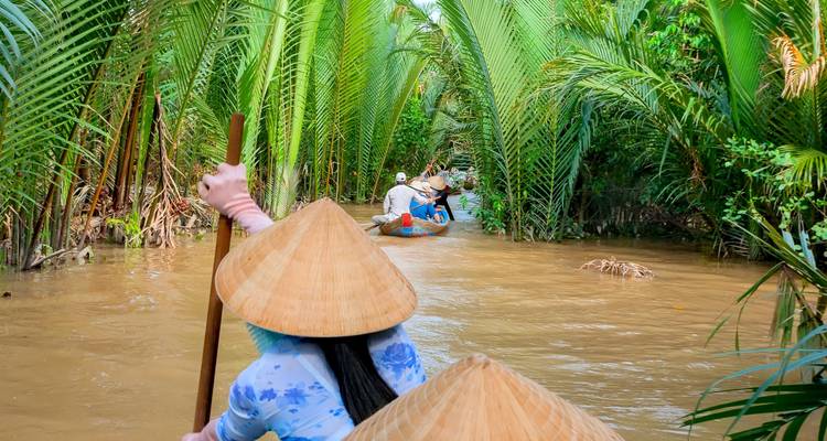 Touristen paddeln in runden Booten durch einen von Kokospalmen gesäumten Kanal.