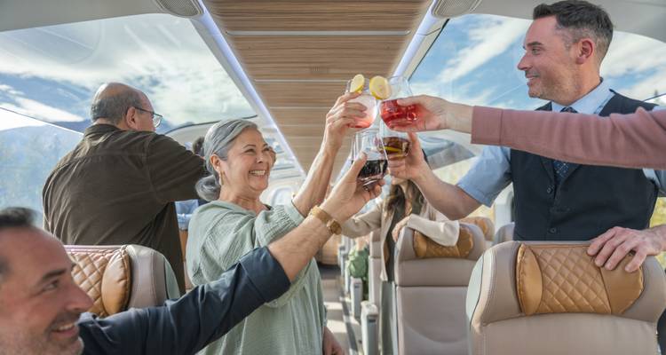 Les passagers lèvent des cocktails colorés dans un toast joyeux à l'intérieur d'une voiture panoramique lumineuse avec des panneaux de toit en verre.