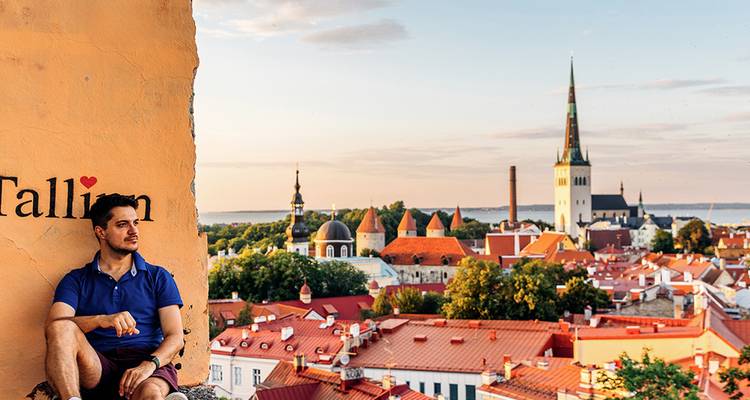 Joven relajándose en una cornisa de piedra con vista al horizonte del Casco Antiguo de Tallin con techos rojos al atardecer.