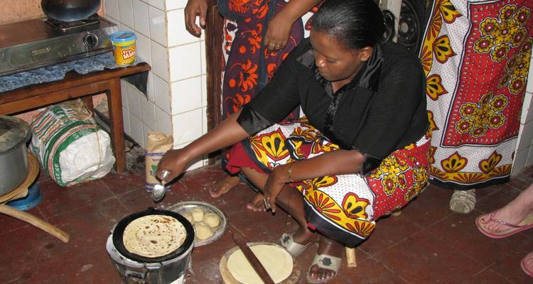 Woman cooking traditional flatbread on a stove in a kitchen setting.