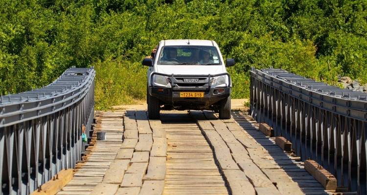 Wit voertuig dat een metalen en houten brug oversteekt