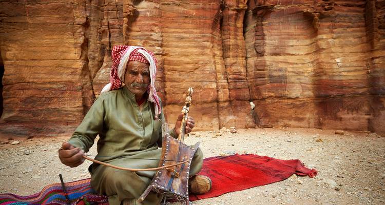 Un musicien jouant d'un instrument devant les formations rocheuses de Pétra.
