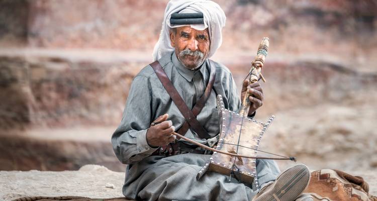 Un homme jouant d'un instrument traditionnel devant les formations rocheuses de Pétra.