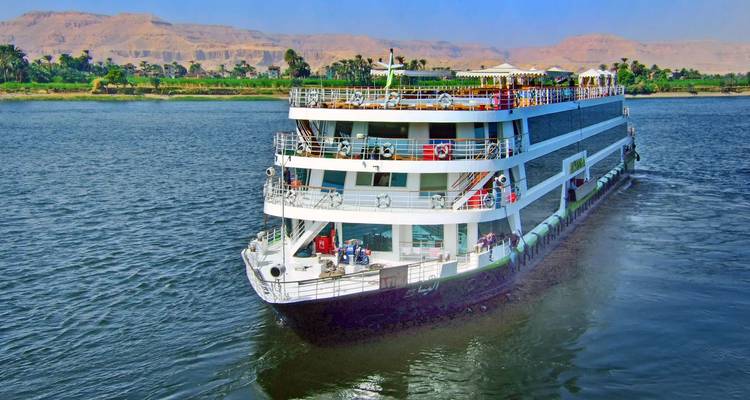 Bateau de croisière naviguant sur le fleuve Nil avec paysage en arrière-plan.