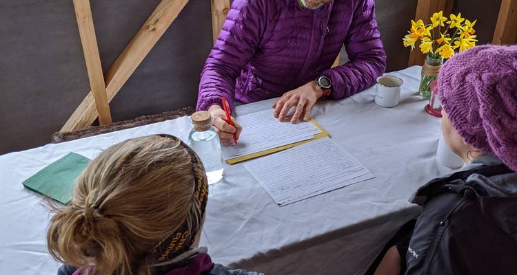 People discussing papers at a table inside wooden structure.