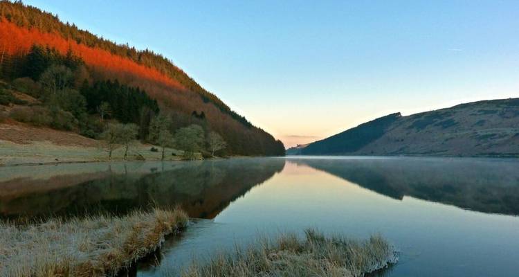 Serene lake with forested hills and frosty shoreline at dawn.