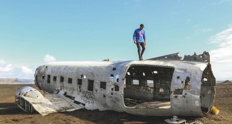 Une personne debout sur l'épave d'un vieil avion sur une plage de sable noir.