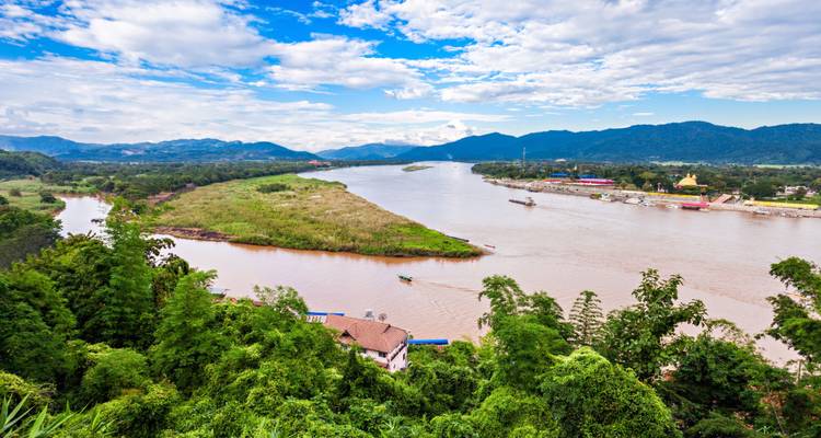 Gouden Driehoek met boten op een zandige rivieroever omringd door weelderige heuvels.