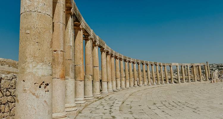 La larga columnata curva del foro romano de Jerash se extiende bajo un cielo azul profundo sin nubes.