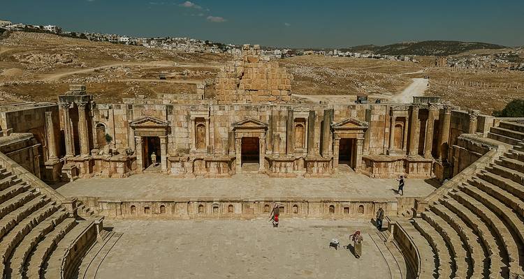Vista amplia del gran anfiteatro de piedra de Jerash y el escenario rodeados de colinas ondulantes.