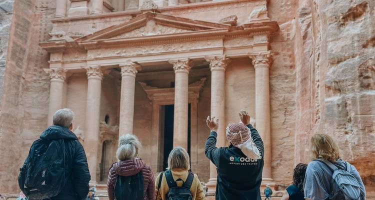 Los viajeros están frente al icónico Tesoro de Petra mientras su guía levanta los brazos para explicar.