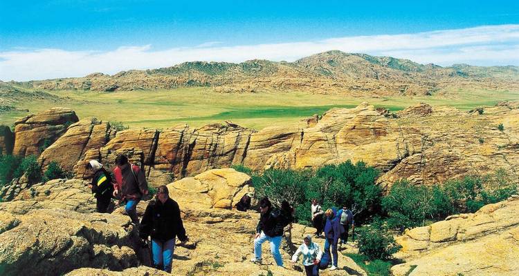 Un grupo de personas haciendo senderismo en terreno rocoso con un vasto paisaje de fondo.