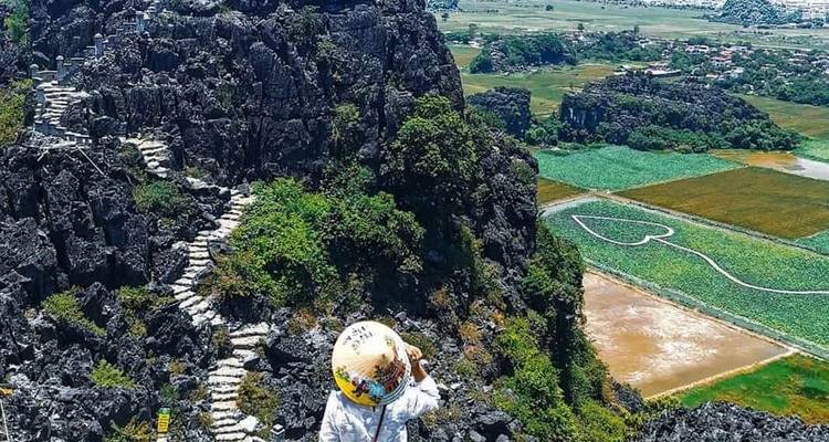 Personne prenant une photo sur un escalier rocheux avec des champs en arrière-plan.