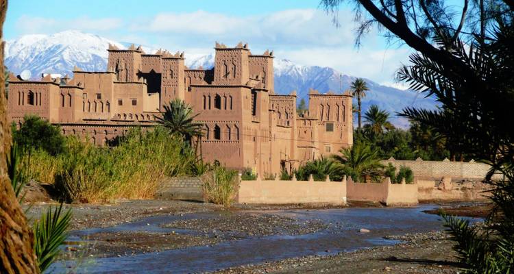 Kasbah marroquí tradicional con montañas nevadas al fondo.