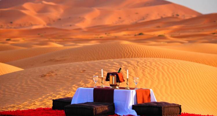 Configuración de picnic en el desierto con mesa y cojines en dunas de arena.