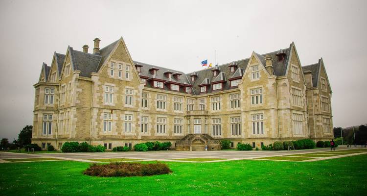 A large stone building surrounded by green lawns and cloudy skies.