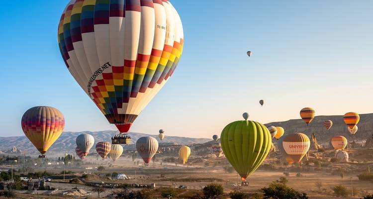 Veel heteluchtballonnen in de lucht boven een rotsachtig landschap in Cappadocië.