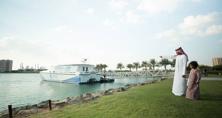 Man en kind wijzen naar een boot bij het water met palmbomen.