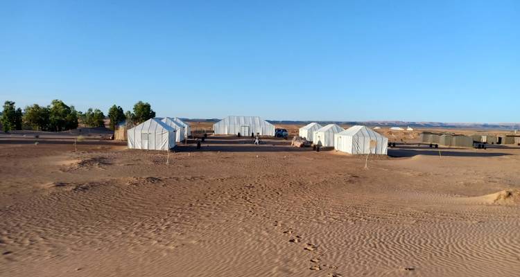 Campement dans le désert avec des tentes blanches pendant la journée.