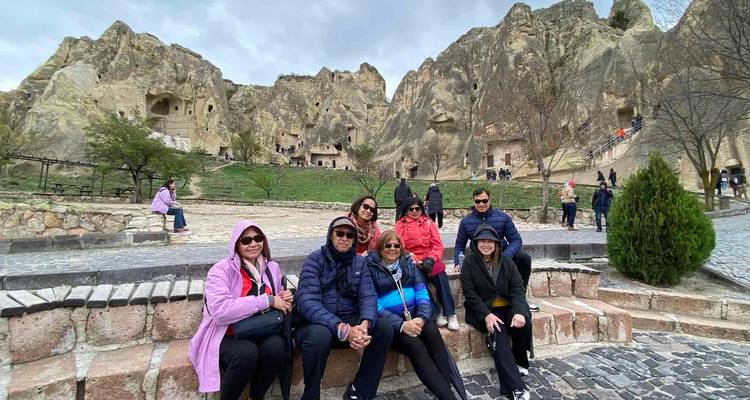 Grupo sentado en bancos de piedra con viviendas excavadas en la roca detrás.