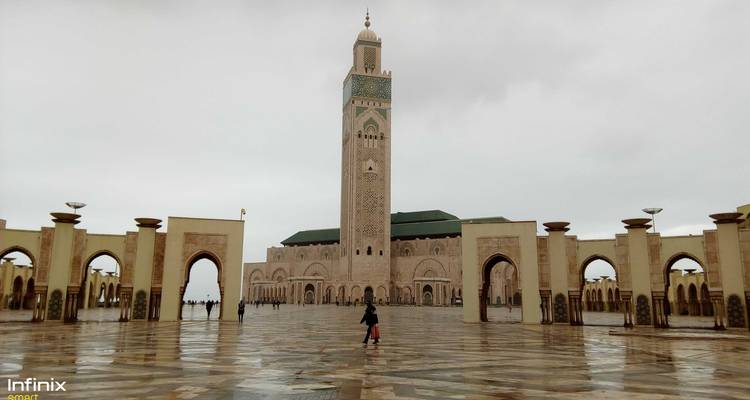 Grote moskee met minaret, met mensen en reflectie op natte grond.