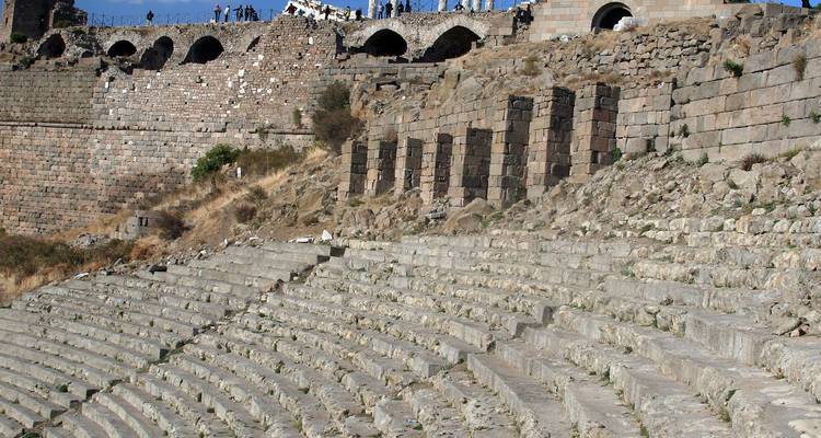 Stone seating of an ancient hillside amphitheater with visitors walking along the top in Pergamon.