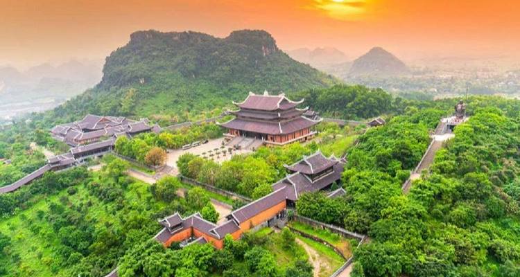 Bai Dinh tempelcomplex tijdens zonsondergang, omgeven door groene heuvels.