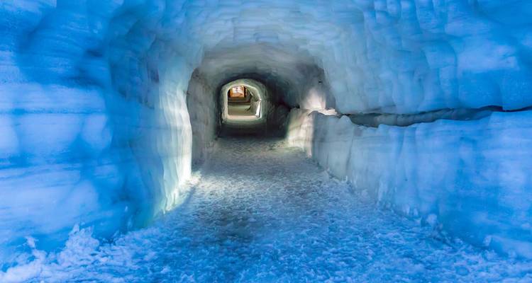 Eisig blauer, künstlich angelegter Tunnel in einem Gletscher, beleuchtet durch sanftes Licht.