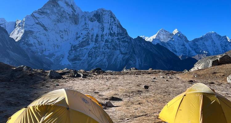 Kampeerterrein met gele tenten met uitzicht op besneeuwde bergen.