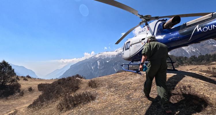 Persoon die naar een helikopter loopt die geparkeerd staat op een bergrand.