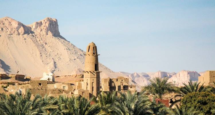 Antike Ruinen mit einer bergigen Kulisse und einem hohen runden Turm.