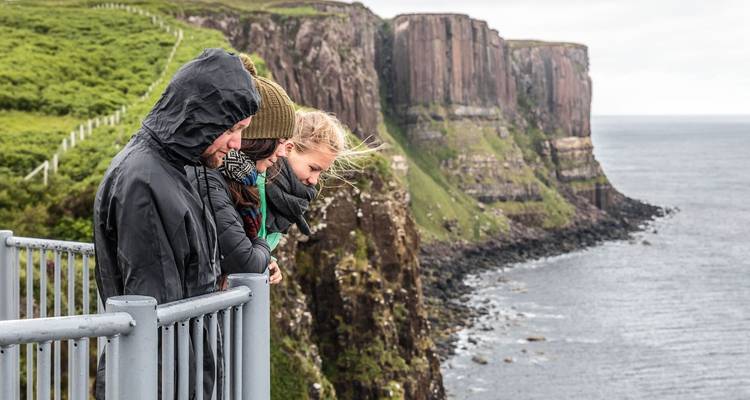 Des voyageurs se penchent par-dessus une balustrade au bord d'une falaise en regardant vers le bas les falaises marines escarpées et l'océan.