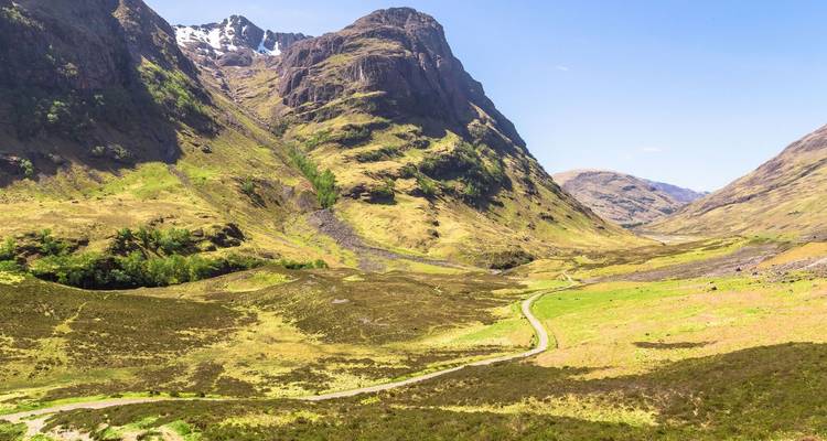 La vallée verdoyante de Glencoe serpente entre des pics escarpés et accidentés sous un ciel clair.