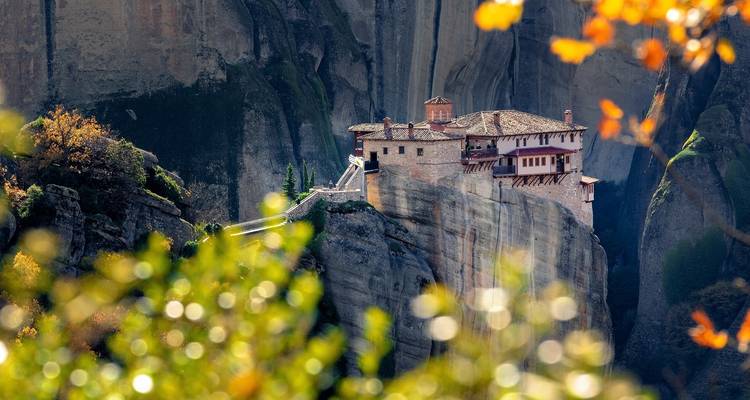 Kloster auf felsigen Klippen, umgeben von Herbstlaub.