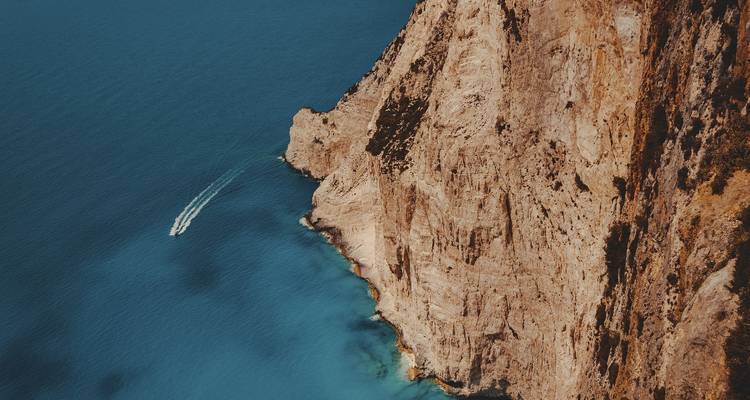 Vogelperspektive von einer Klippe und dem Ozean mit einem Boot.