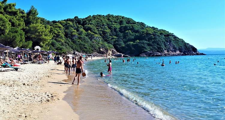 Zandstrand met mensen die zwemmen en luieren aan zee.