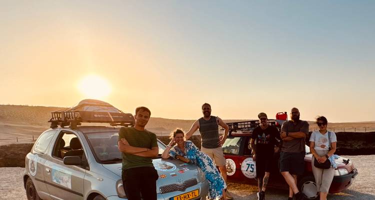 Groupe de voyageurs s'appuyant sur des voitures de rallye posant au coucher du soleil dans un vaste désert.
