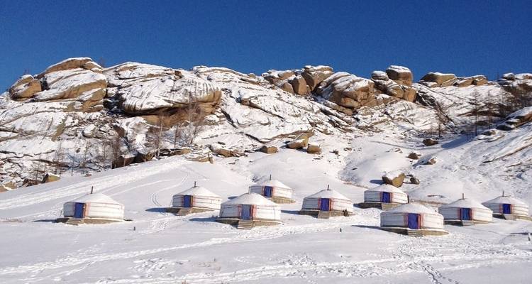 Plusieurs yourtes mongoles traditionnelles installées dans un paysage enneigé.