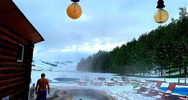 Personne dans une source chaude avec un paysage enneigé et une forêt en arrière-plan.